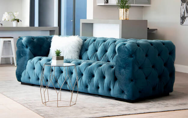Teal velvet buttoned upholstered couch on a grey rug in living room setting